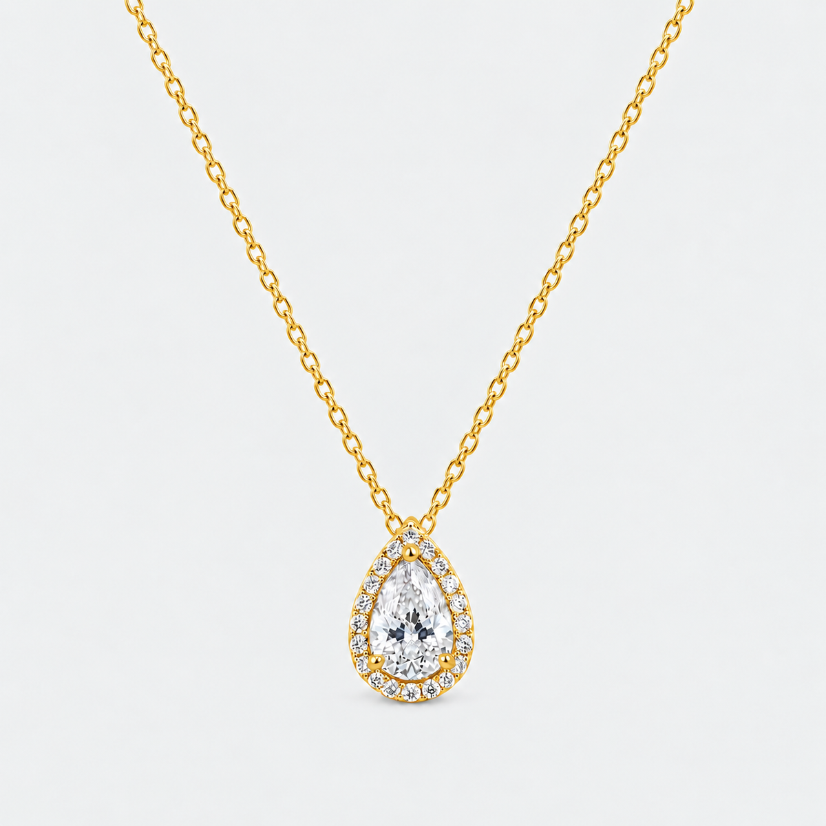 A gold chain necklace with a teardrop-shaped pendant featuring a large clear central gemstone surrounded by a halo of smaller stones, shown on a light gray background.