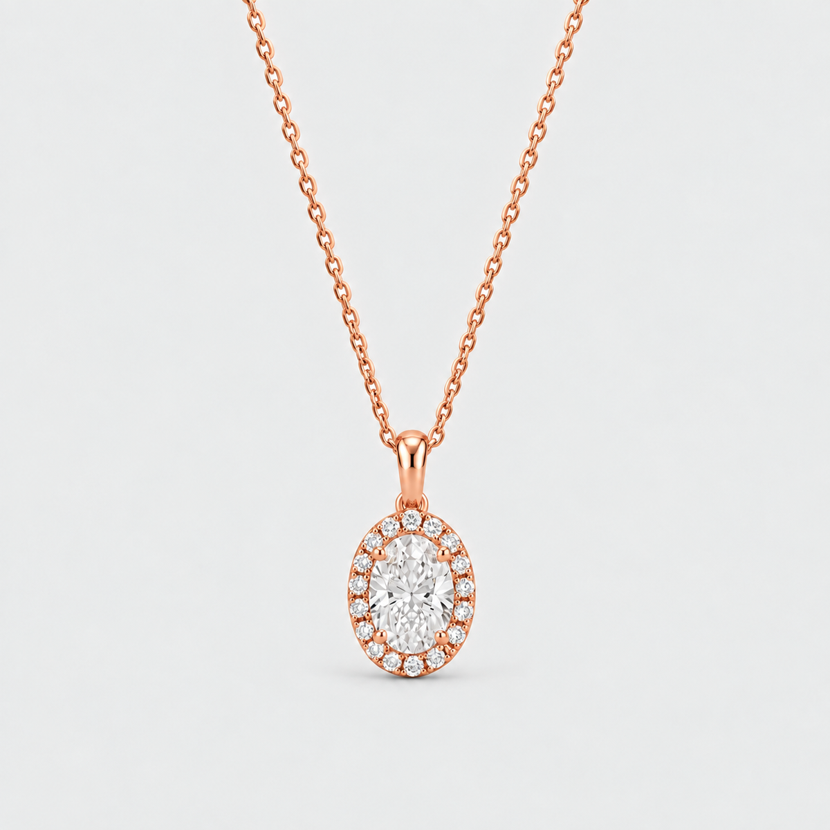 An oval halo pendant necklace in rose gold, featuring a central round-cut clear gemstone surrounded by a halo of smaller clear stones, suspended from a delicate rose gold chain against a light gray background.