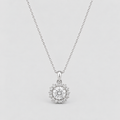 A silver pendant necklace featuring a round-cut clear center stone surrounded by a halo of smaller stones, suspended from a delicate silver chain against a light gray background.
