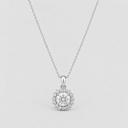 A silver pendant necklace featuring a round-cut clear center stone surrounded by a halo of smaller stones, suspended from a delicate silver chain against a light gray background.