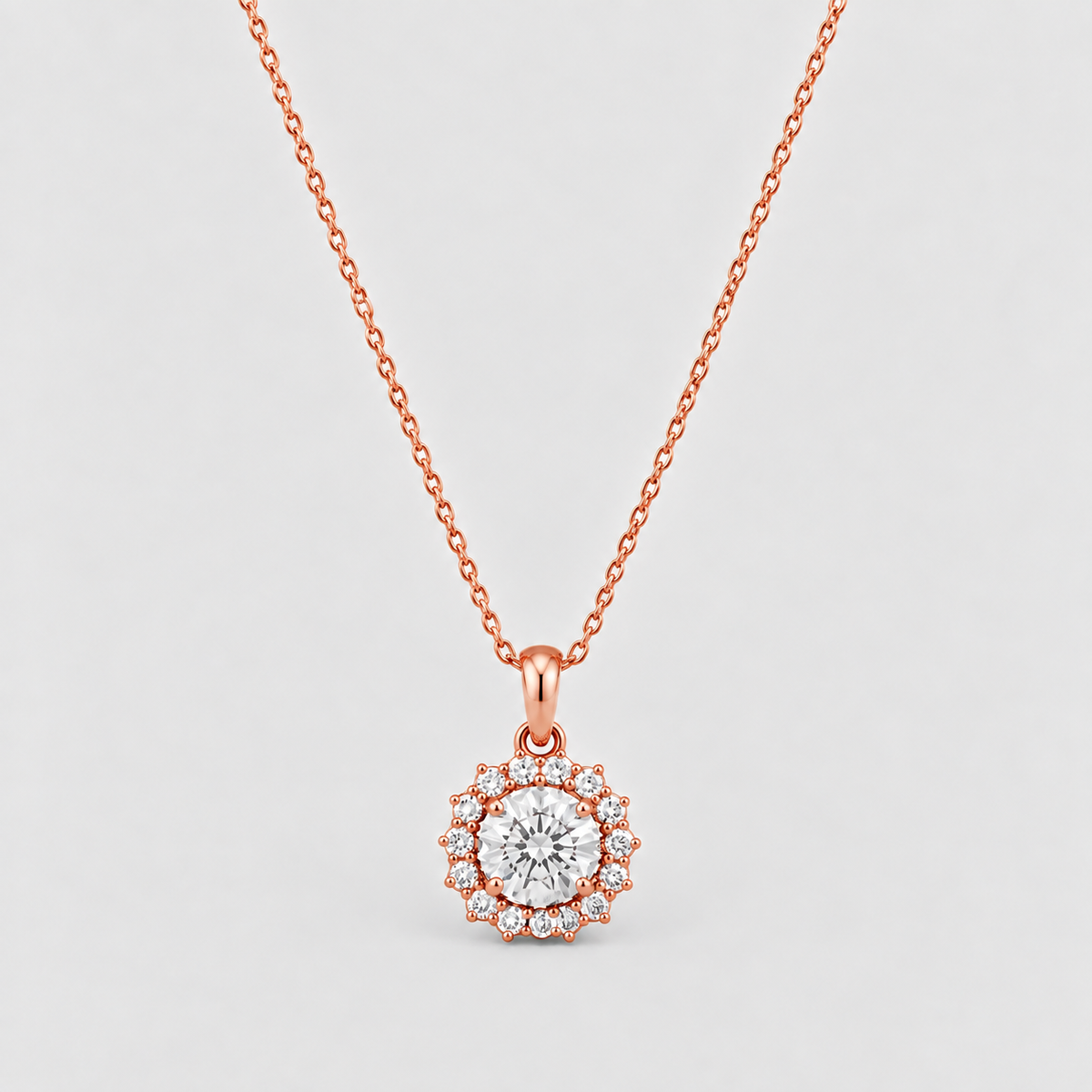 A rose gold necklace with a circular pendant featuring a central round clear gemstone surrounded by a halo of smaller clear stones, suspended from a delicate rose gold chain against a light gray background.