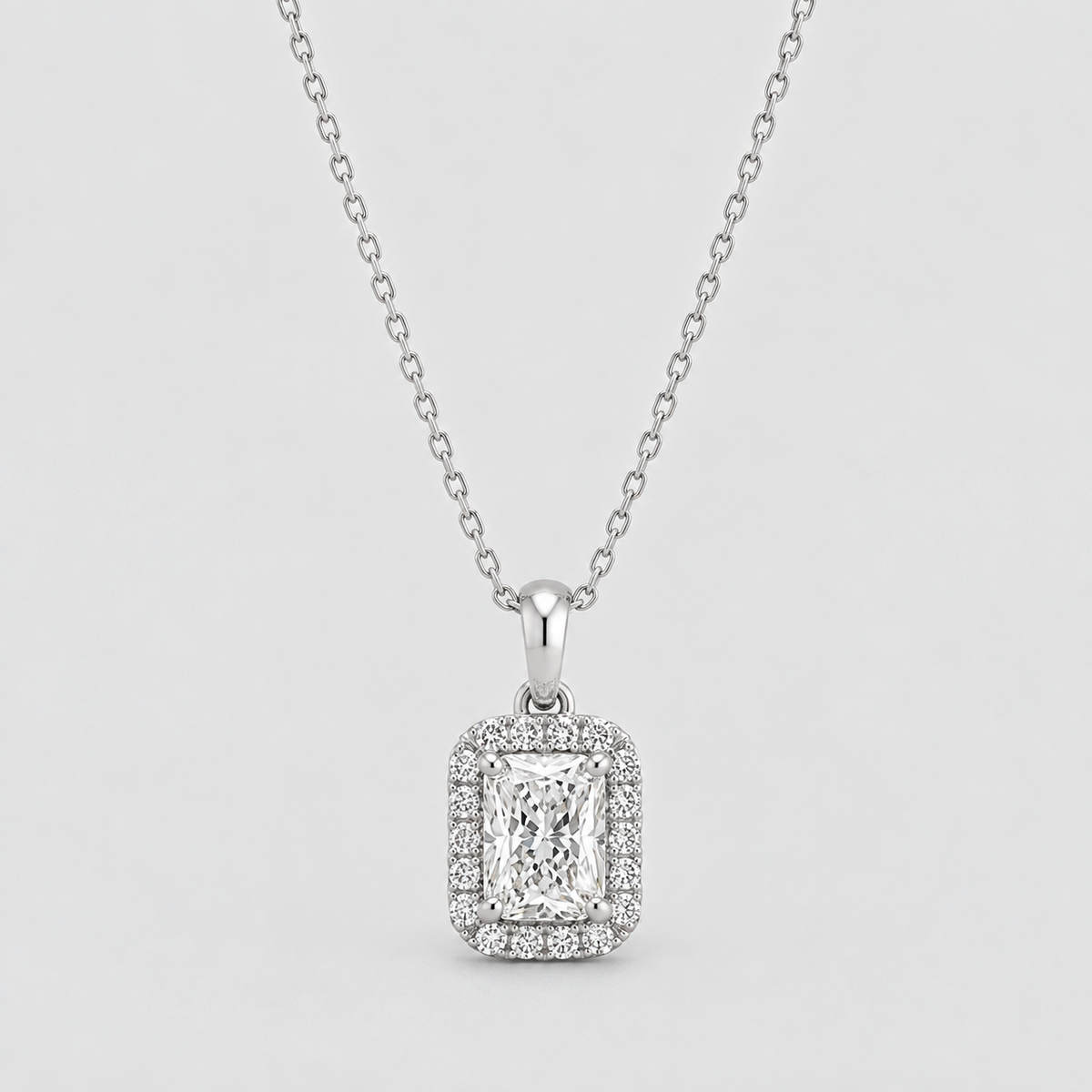 A silver-toned diamond necklace featuring an emerald-cut halo pendant, displayed against a light gray background.