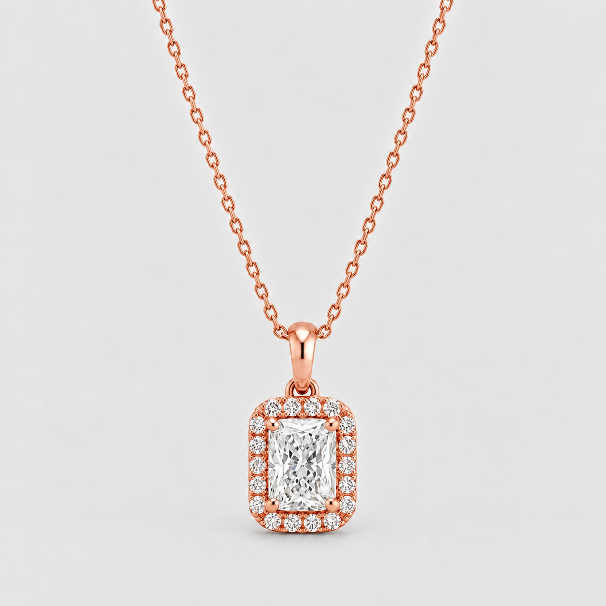 A rose gold necklace with a rectangular halo pendant featuring a central emerald-cut diamond surrounded by smaller round diamonds, shown on a light gray background.