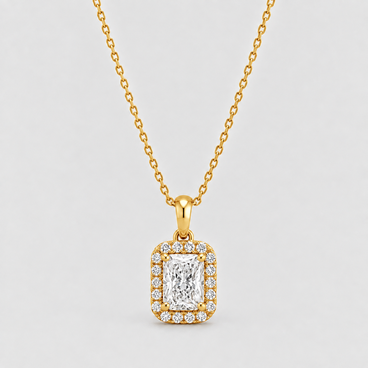 A yellow gold necklace with a rectangular halo pendant featuring a central emerald-cut diamond surrounded by smaller diamonds, shown on a light gray background.