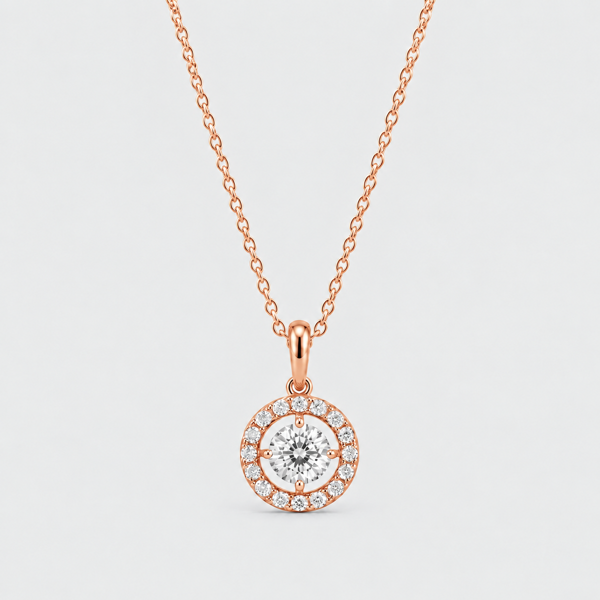 A rose gold pendant necklace featuring a round-cut center stone surrounded by a halo of small pavé-set stones, suspended from a delicate rose gold chain against a light gray background.