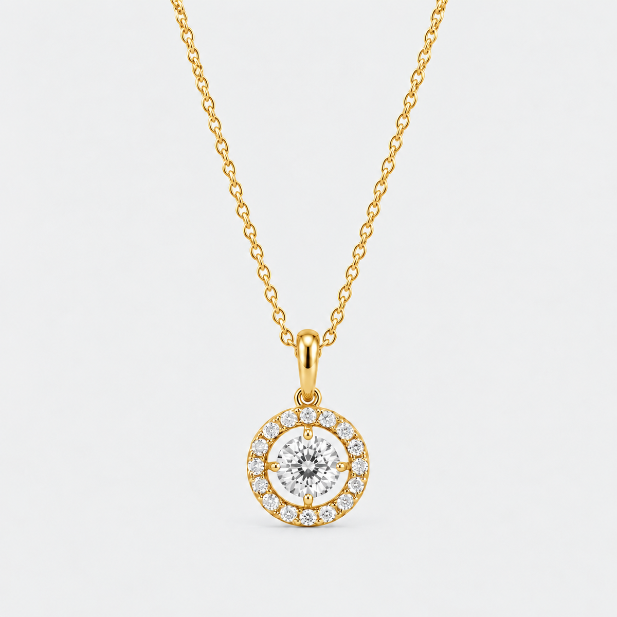 A gold chain necklace with a round pendant featuring a central clear gemstone surrounded by a halo of smaller diamonds, set against a light gray background.