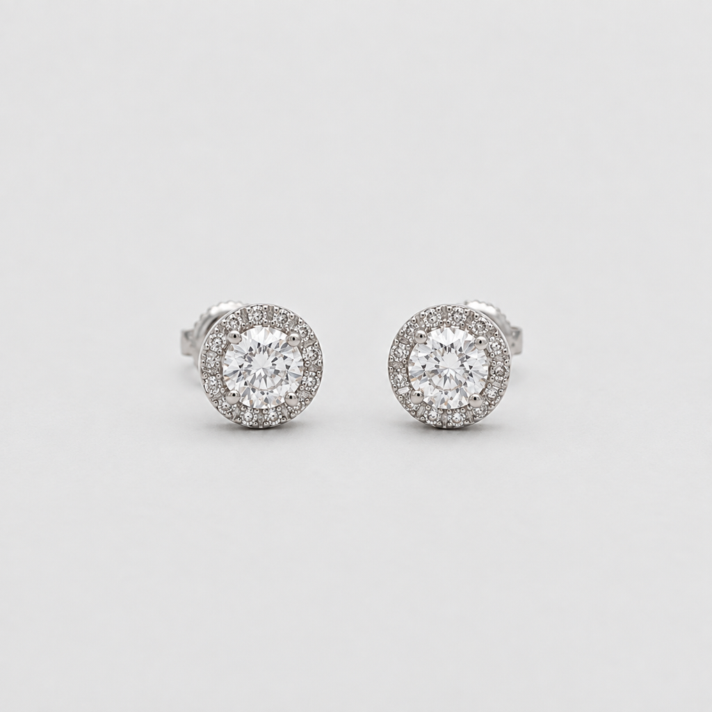A pair of round halo stud earrings in silver-toned metal, featuring a central clear gemstone surrounded by a halo of smaller clear stones, set against a plain light gray background.
