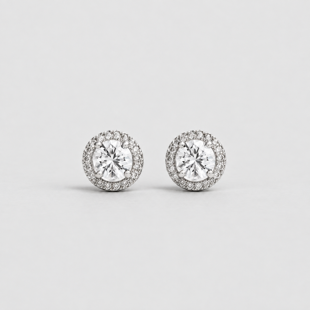 A pair of round halo stud earrings with silver-toned metal settings and clear gemstones, displayed on a light gray background.