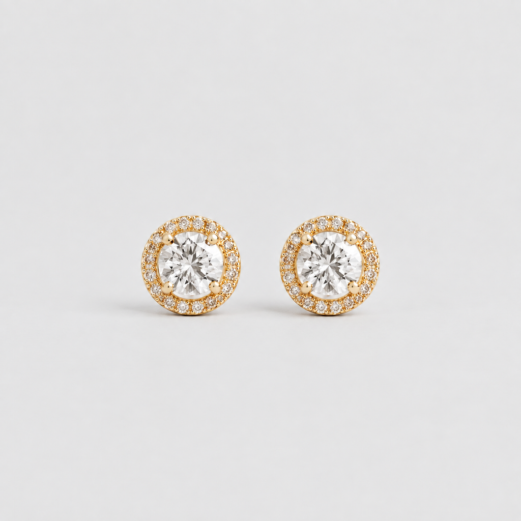 A pair of gold and white gold stud earrings with a central round clear gemstone surrounded by a halo of smaller clear stones, set against a light gray background.