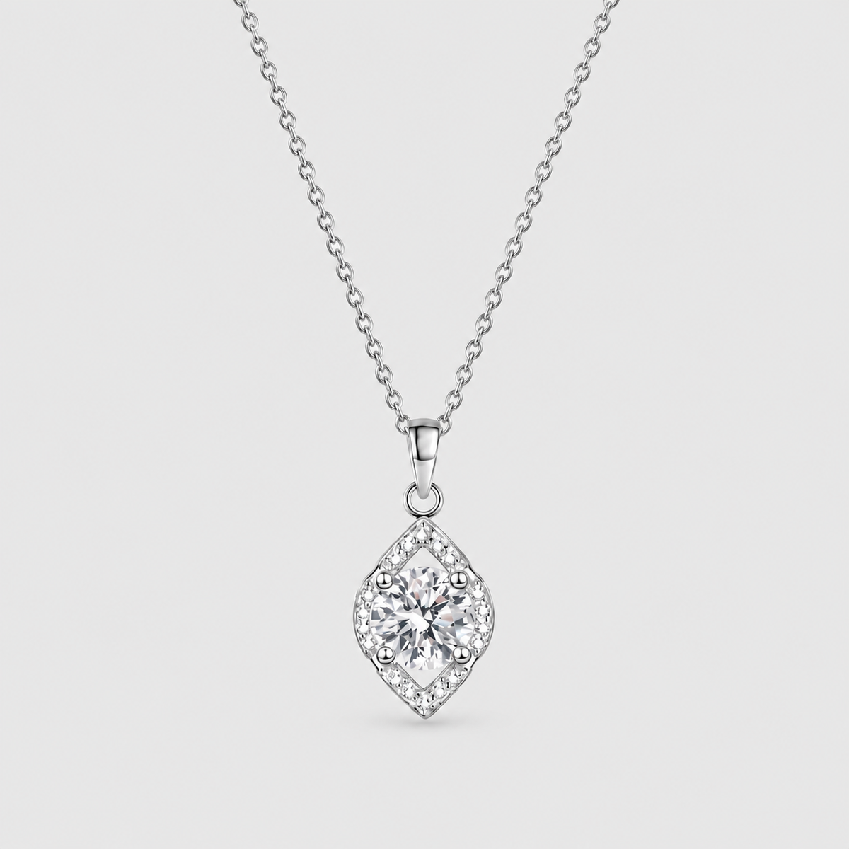 A silver diamond-shaped pendant necklace featuring a central round-cut diamond surrounded by a halo of smaller diamonds, suspended from a delicate silver chain against a light gray background.