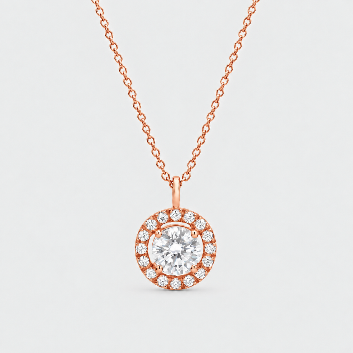 A rose gold pendant necklace featuring a central round clear gemstone surrounded by a halo of smaller pavé-set clear stones, suspended from a delicate rose gold chain against a light gray background.