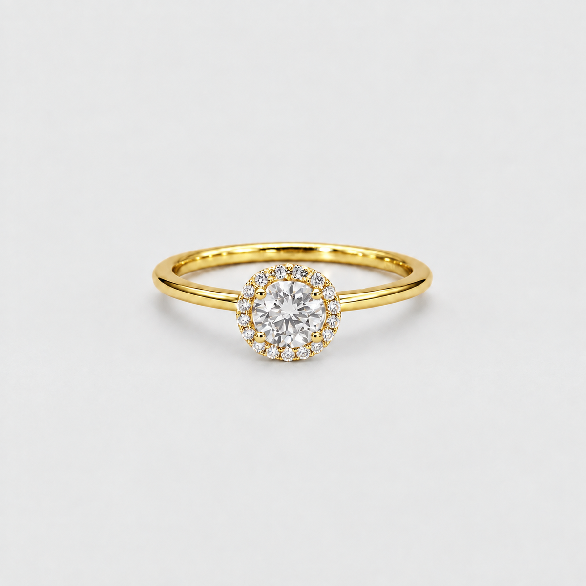 A yellow gold halo ring with a round-cut diamond center stone and smaller accent diamonds, shown on a clean light gray background.