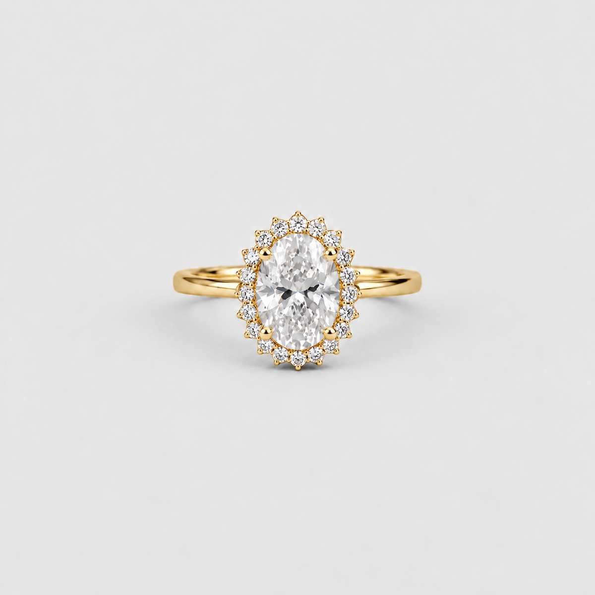 An oval-cut diamond halo ring in yellow gold, featuring a central oval diamond surrounded by a halo of smaller round diamonds, set on a slim yellow gold band against a light gray background.