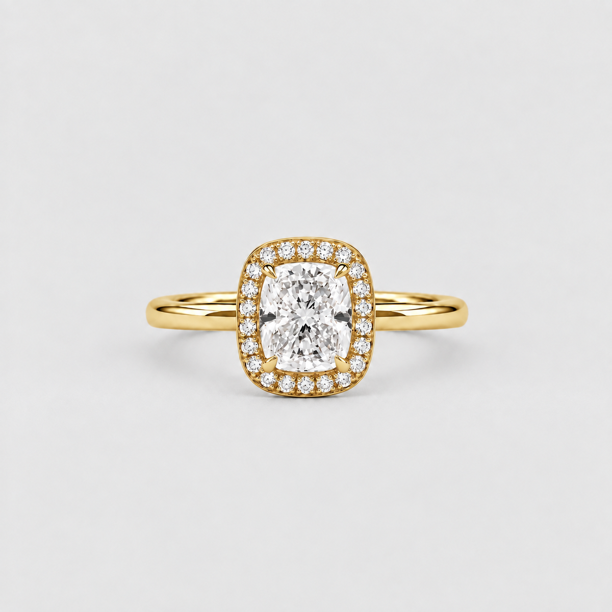 A yellow gold halo ring featuring a cushion-cut diamond center stone surrounded by a halo of smaller round diamonds, set on a plain light gray background.