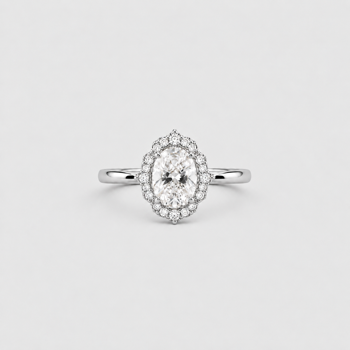 An oval halo ring featuring a brilliant-cut center stone surrounded by a double halo of smaller round stones, set on a polished silver-colored band, shown against a light gray background.