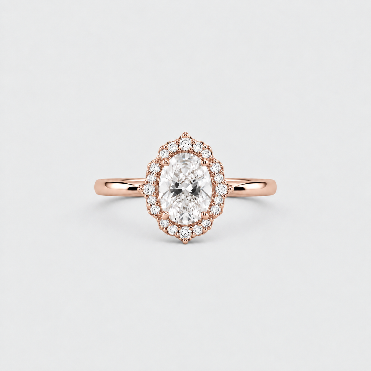 A rose gold halo ring featuring an oval-cut center stone surrounded by a double row of small round-cut stones, set against a clean light gray background.