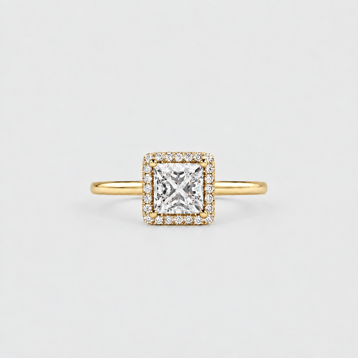 A yellow gold halo ring featuring a princess-cut diamond center stone surrounded by a halo of small diamonds, set on a plain light gray background.