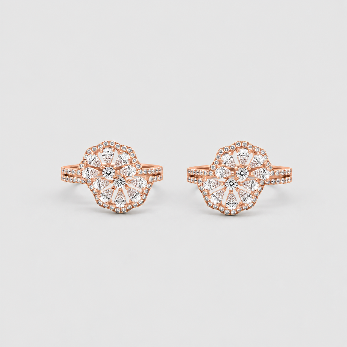 A pair of rose gold rings with intricate floral cluster settings paved with small clear stones, displayed on a light gray background.