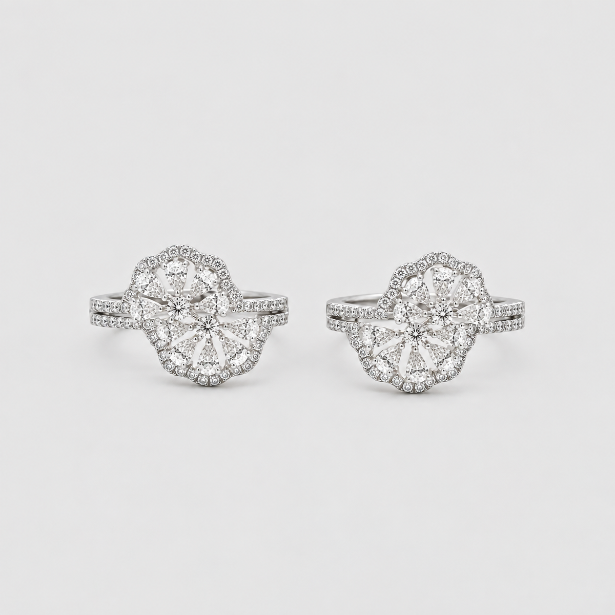 A pair of silver-toned halo rings with large round-cut center stones and rows of smaller accent stones, photographed on a clean light gray background.