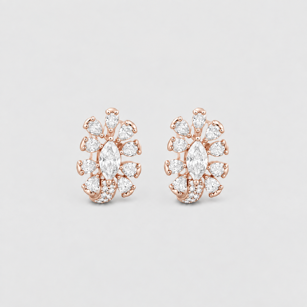A pair of rose gold huggie earrings featuring marquise-cut and round-cut clear gemstones in a floral cluster setting, displayed on a light gray background.