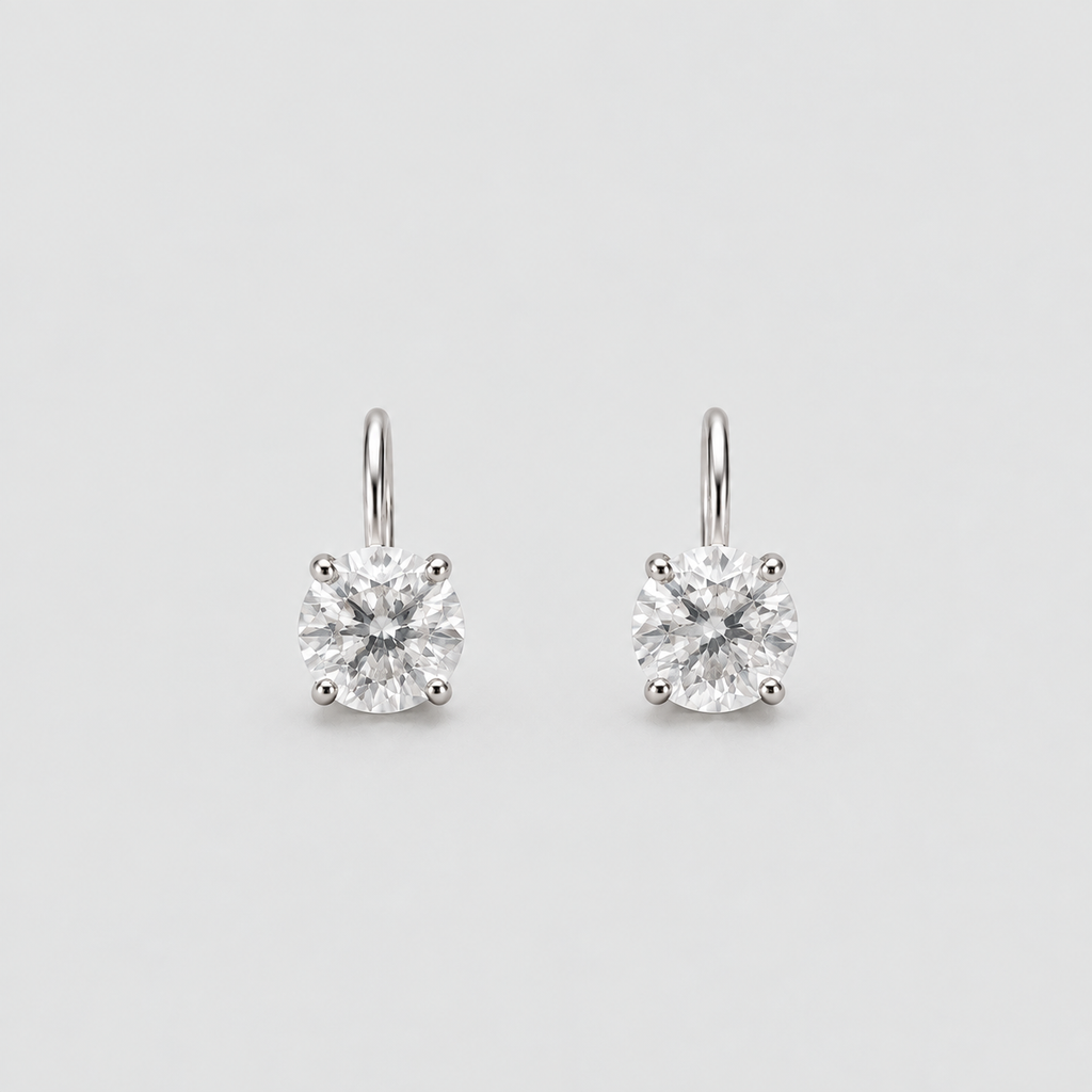 A pair of solitaire drop earrings with round brilliant-cut clear gemstones in a silver-toned four-prong setting, suspended from simple silver-toned hooks against a light gray background.