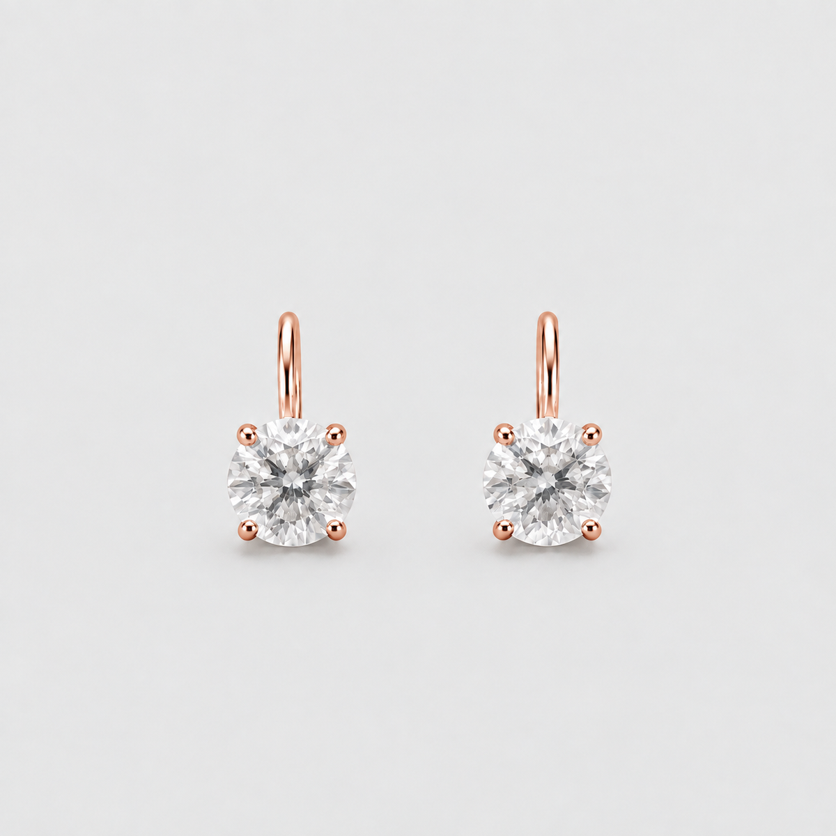 A pair of rose gold stud earrings with round-cut clear gemstones in four-prong settings, shown on a light gray background.
