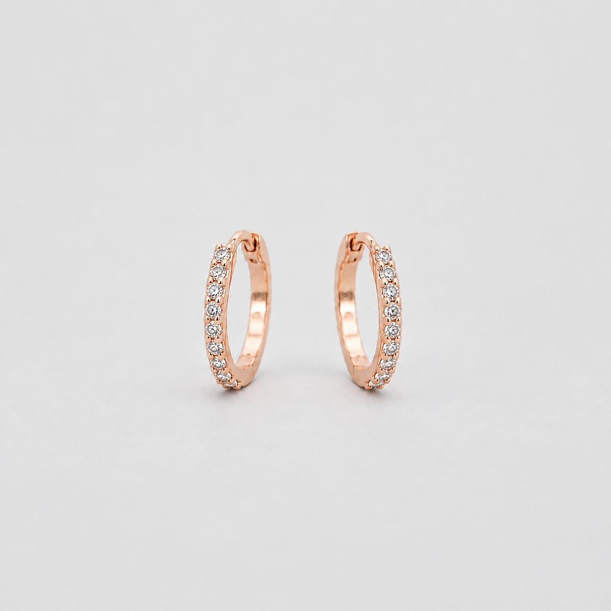 A pair of small rose gold hoop earrings with pavé-set clear stones, displayed on a clean light gray background.