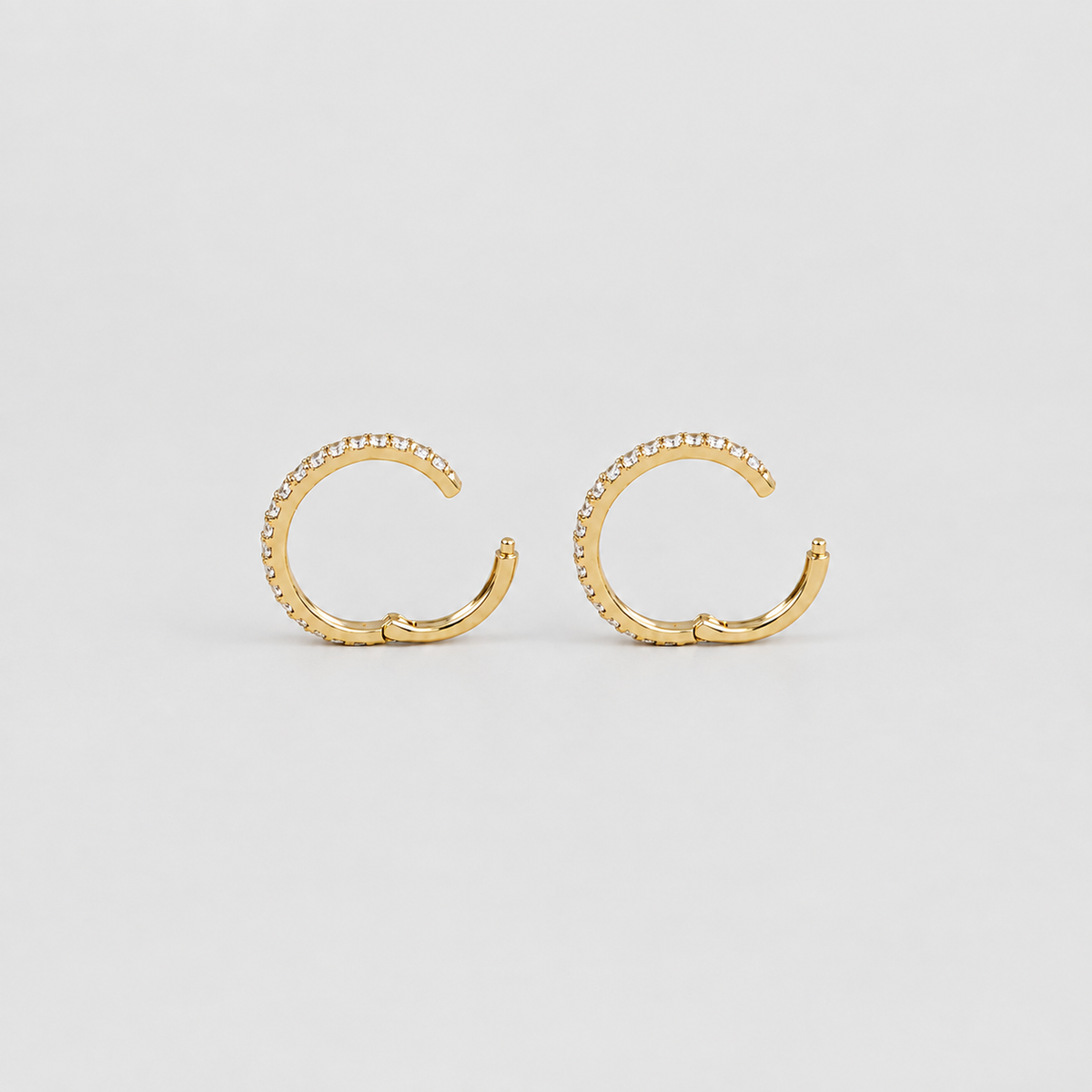 A pair of gold huggie hoop earrings with a textured, beaded outer edge and a smooth hinge clasp, displayed on a light gray background.