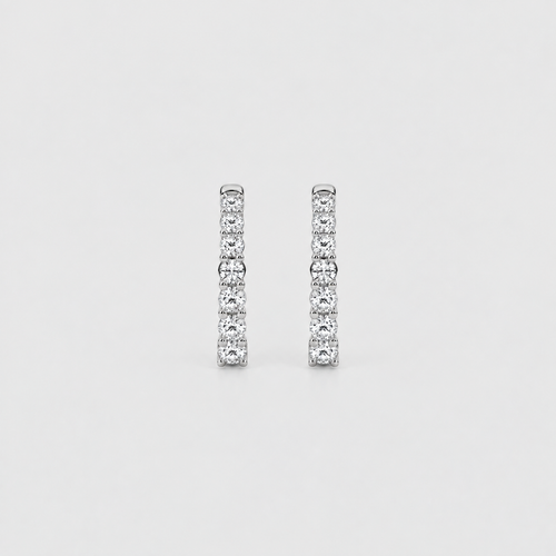 A pair of silver-toned huggie hoop earrings set with round-cut clear gemstones, shown against a light gray background.