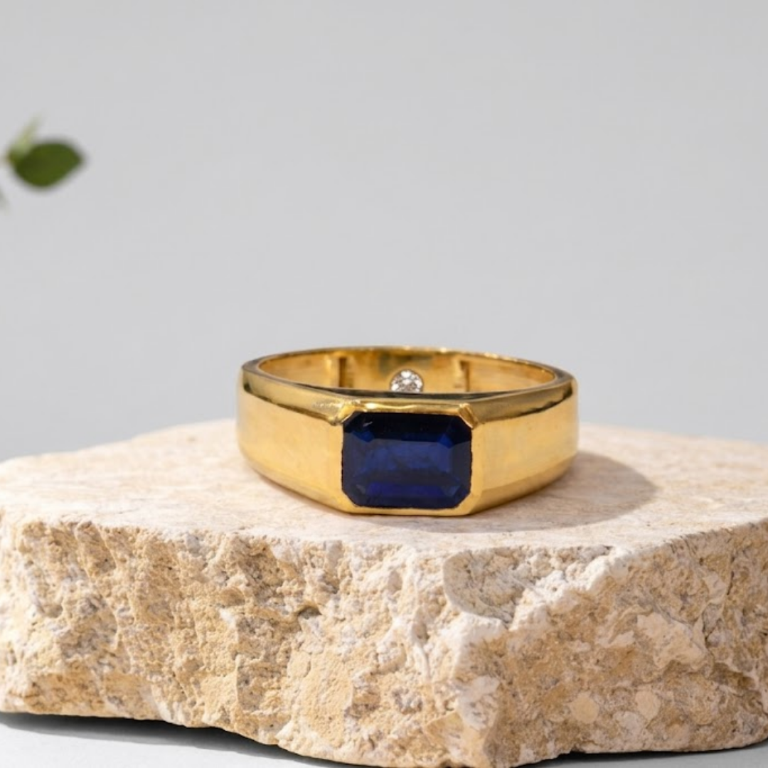 Gold ring with a blue gemstone on a stone surface with a light gray background