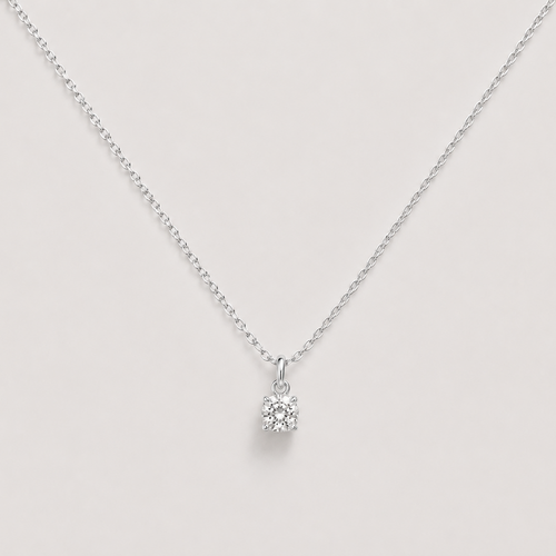 A delicate silver chain necklace with a small, clear gemstone pendant set in a silver bezel, displayed against a solid light beige background.