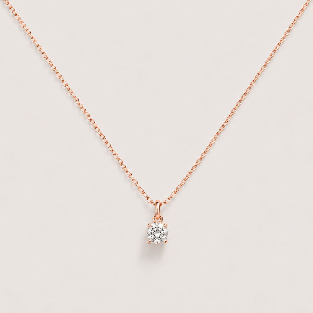 A delicate gold chain necklace with a small, clear gemstone pendant set in a gold bezel, displayed against a light gray background.