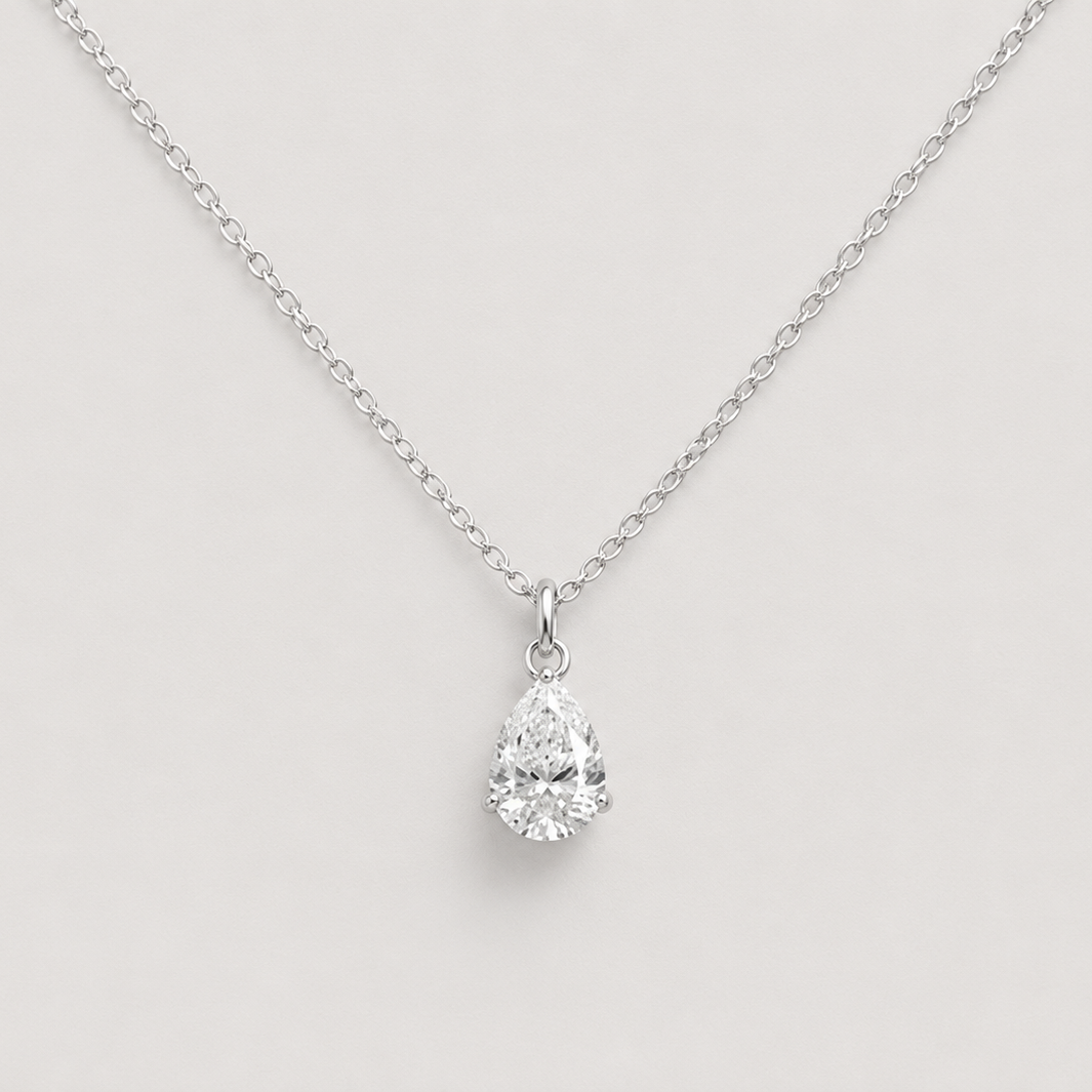 A silver chain necklace with a pear-cut clear gemstone pendant, displayed against a light gray background.
