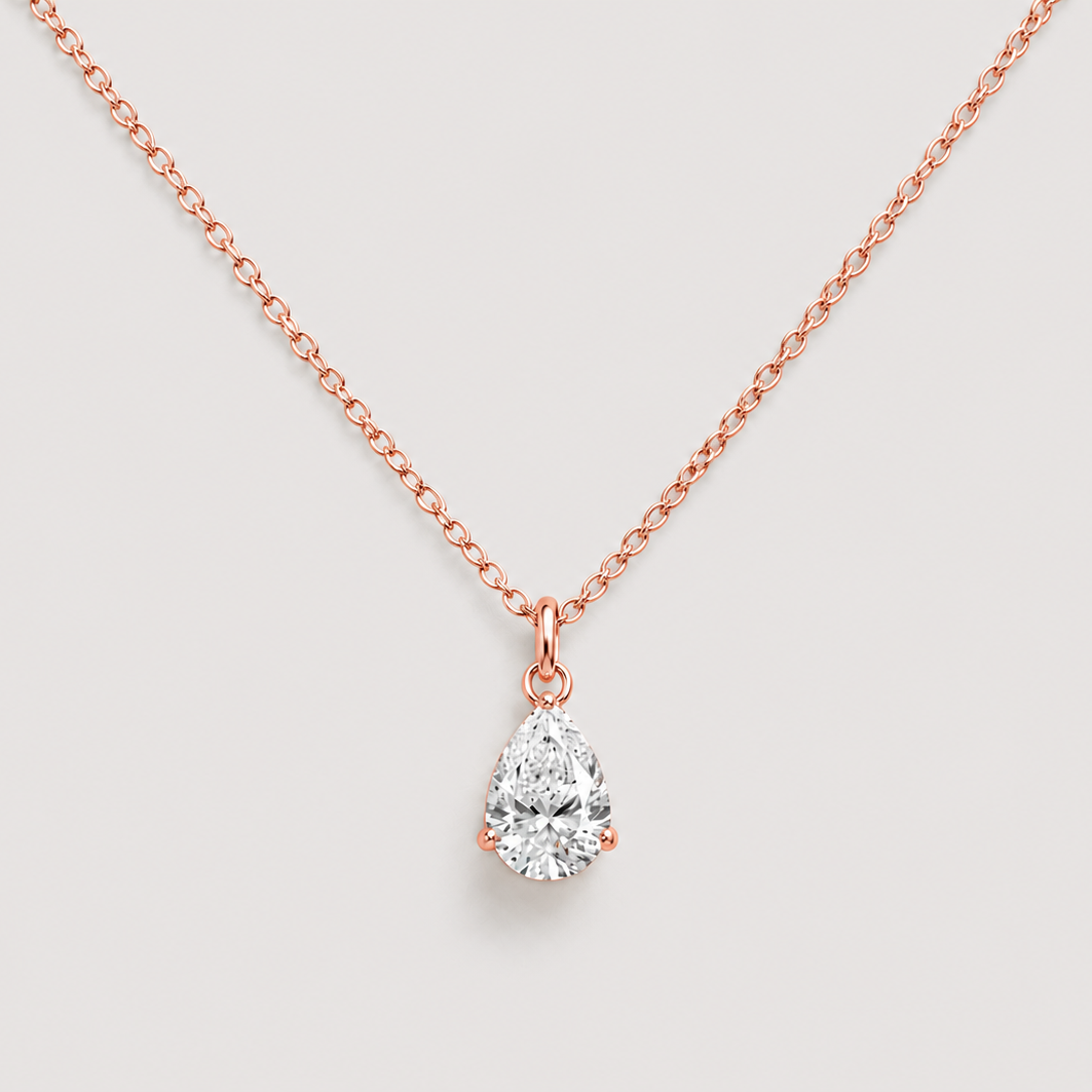 A rose gold necklace with a pear-cut diamond pendant, displayed against a light gray background.