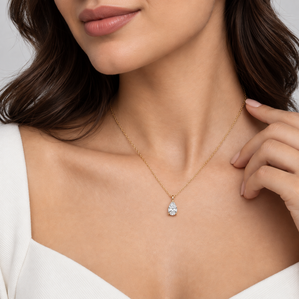 A Model wear pear-cut diamond pendant necklace in a yellow gold setting on a delicate rose gold chain, shown against a clean white background.