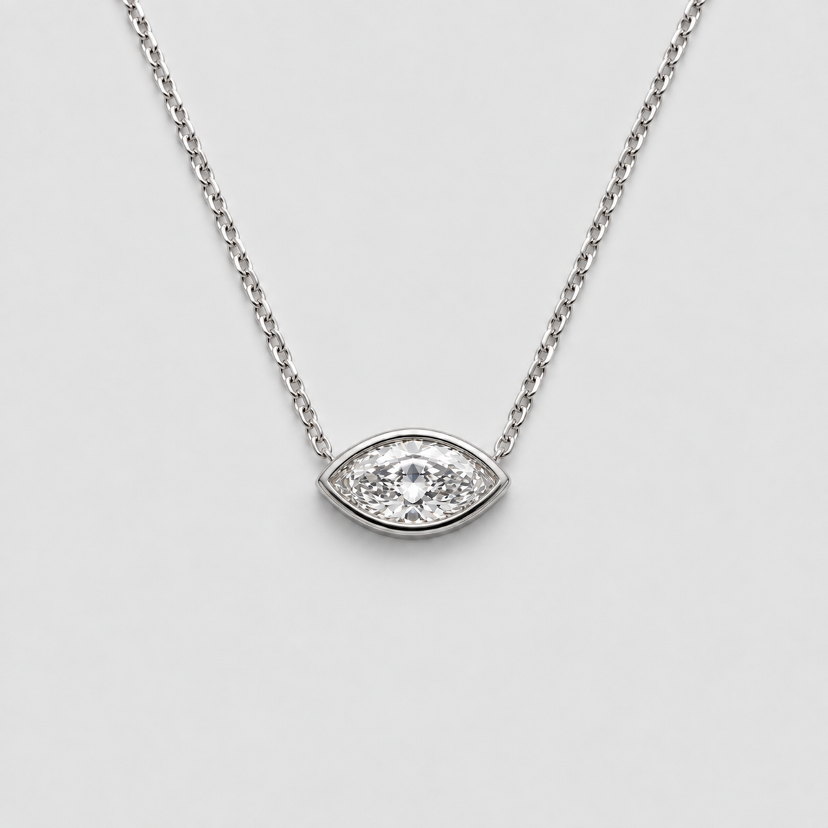 A silver eye-shaped pendant necklace with a clear central gemstone and small surrounding stones, suspended on a delicate silver chain against a light gray background.