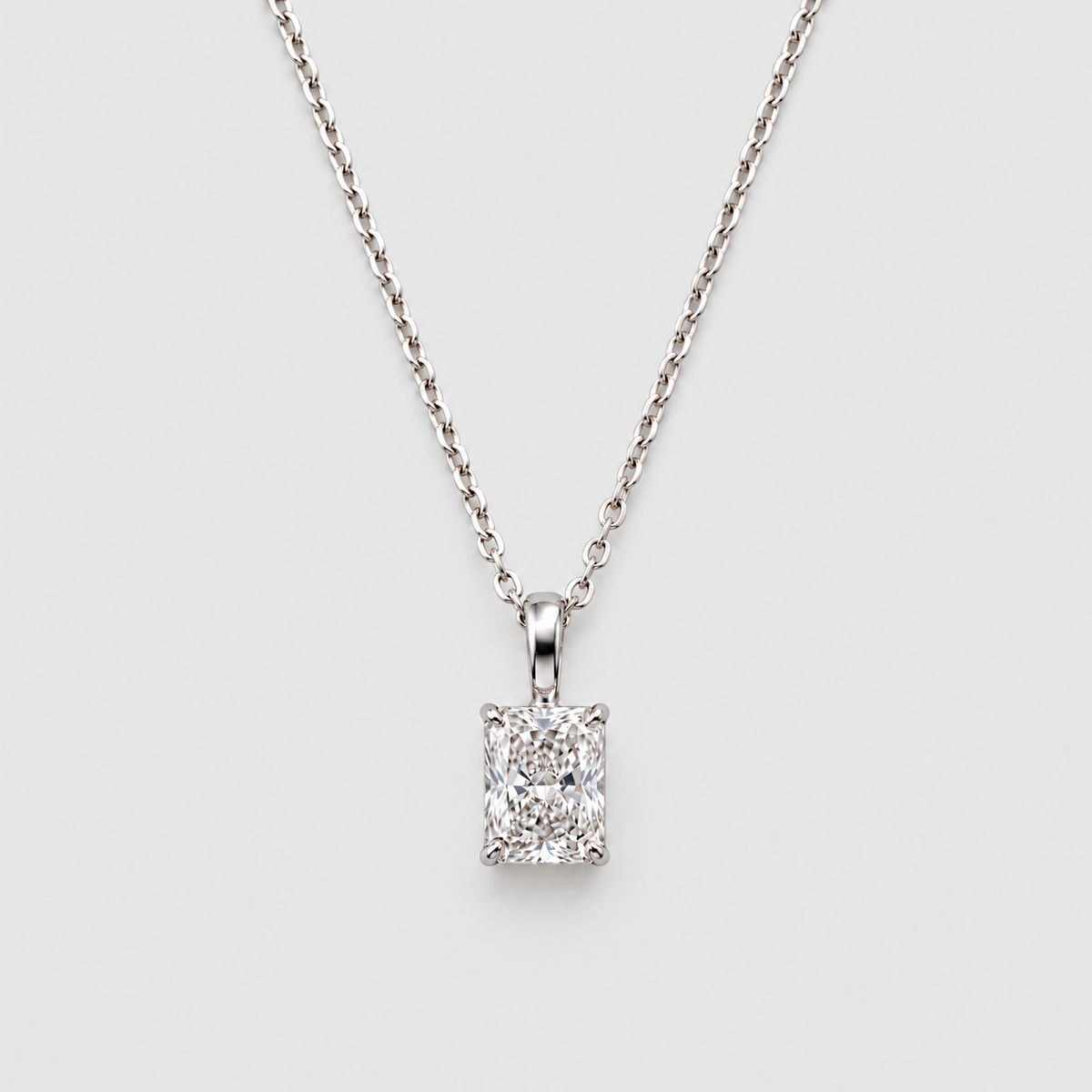A silver-toned necklace with a rectangular emerald-cut diamond pendant, displayed against a clean light gray background.