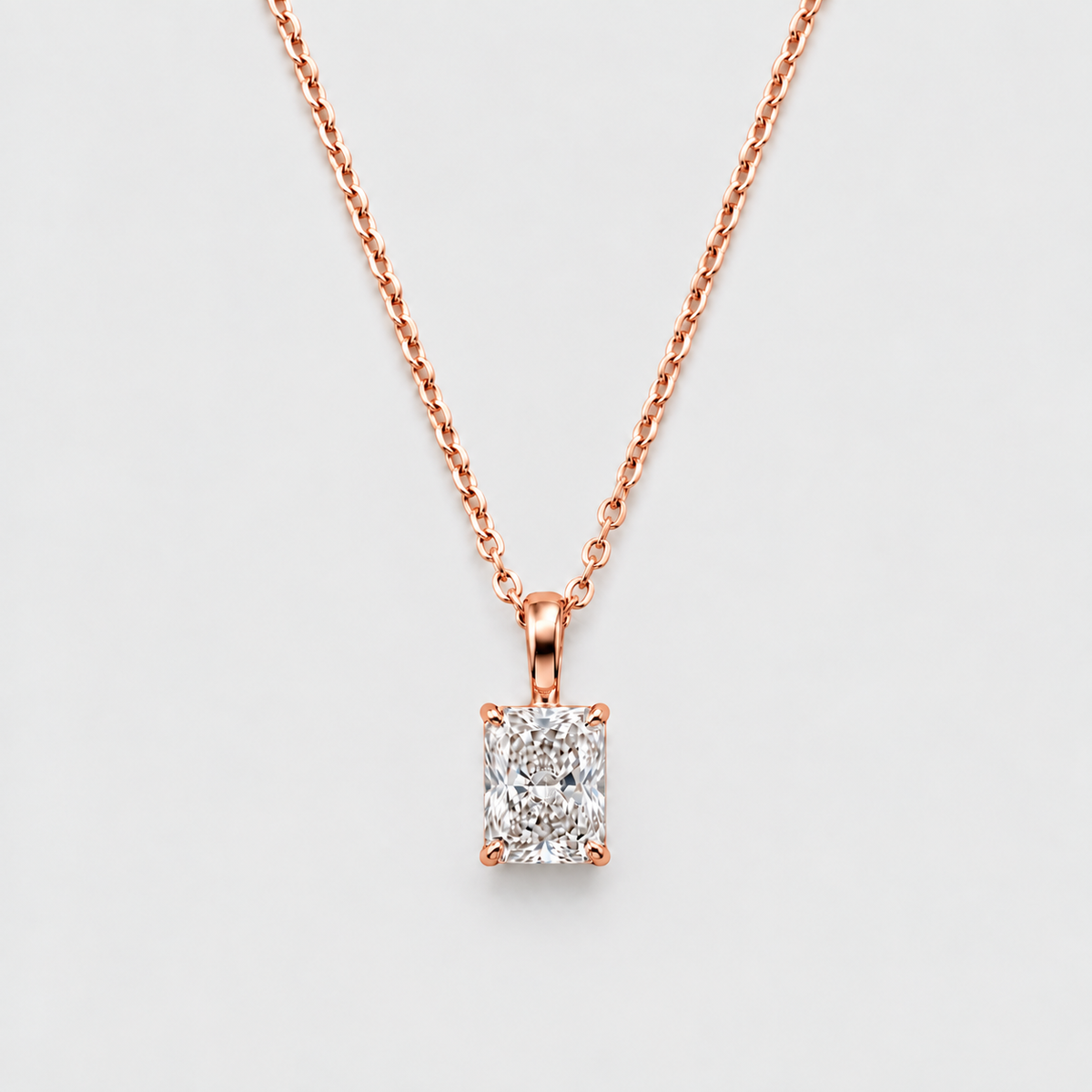 A rose gold necklace with a rectangular emerald-cut diamond pendant, displayed against a clean, light gray background.
