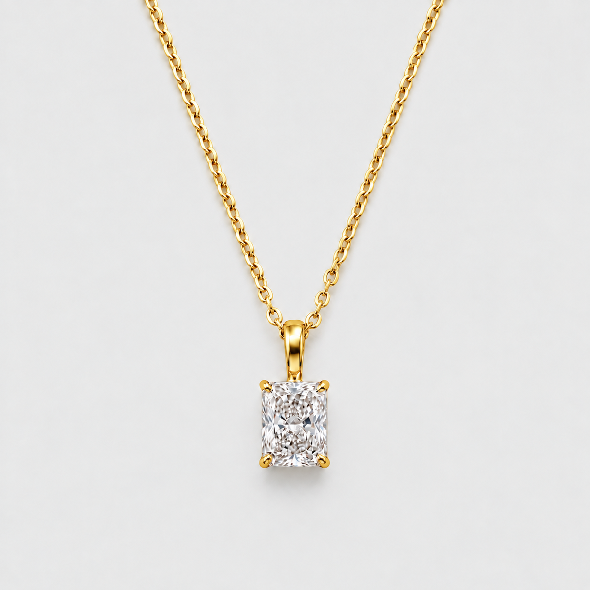 A yellow gold necklace with a rectangular emerald-cut diamond pendant, displayed against a clean light gray background.