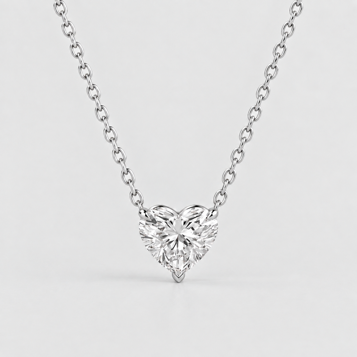 A heart-shaped diamond pendant necklace on a delicate silver chain, photographed against a clean, light gray background.