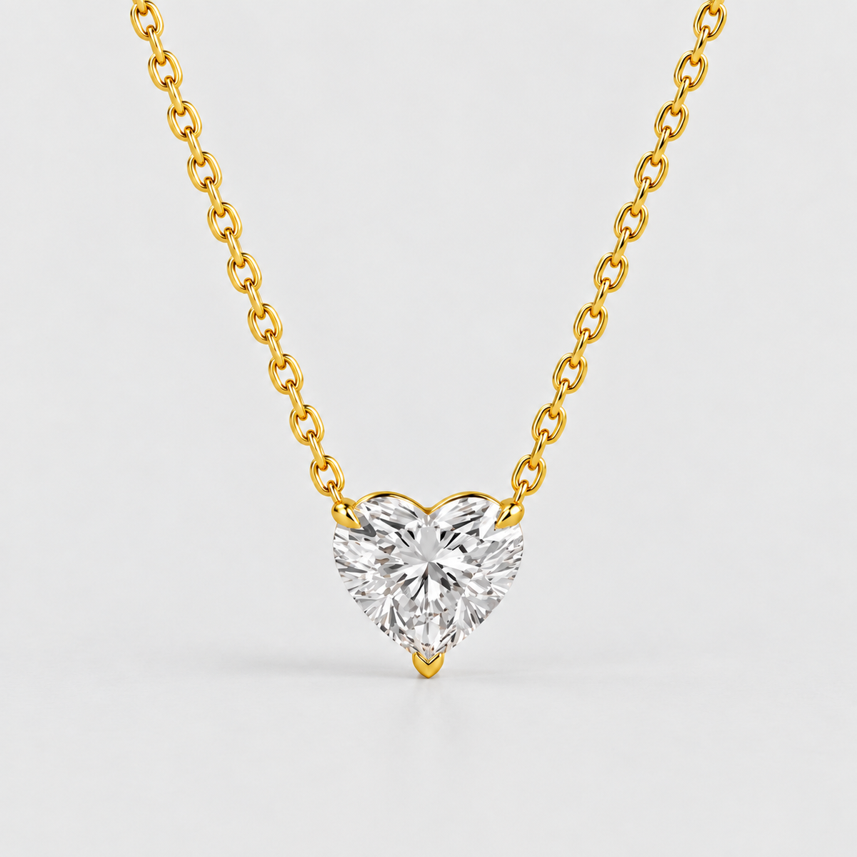 A heart-shaped diamond pendant necklace on a delicate gold chain, set against a clean light gray background.