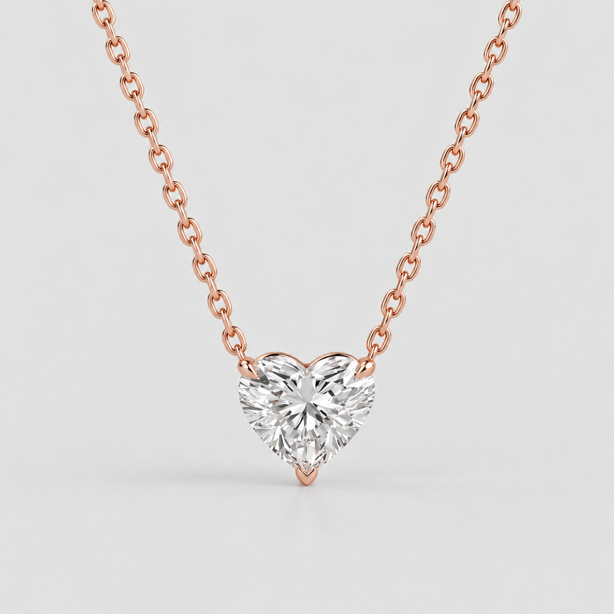 A heart-shaped diamond pendant necklace in a rose gold setting on a matching rose gold chain, shown against a light gray background.
