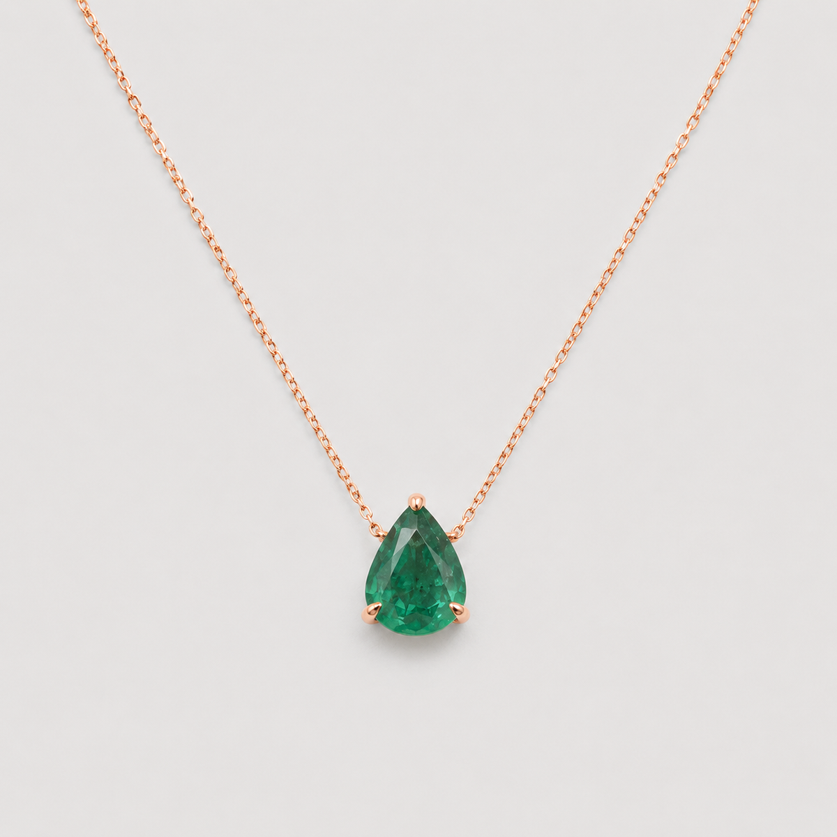 A pear-cut green gemstone pendant necklace in a rose gold setting on a delicate rose gold chain, shown against a light gray background.