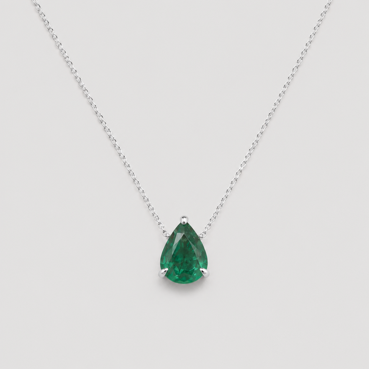 A pear-cut green gemstone pendant necklace in a silver prong setting on a delicate silver chain, shown against a light gray background.