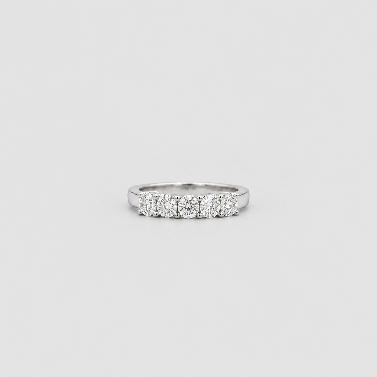 A silver diamond band ring featuring five round-cut diamonds set in a row, photographed against a solid light gray background.