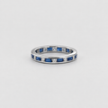 A silver eternity ring featuring baguette-cut blue sapphires and small round-cut clear stones, shown on a neutral light gray background.