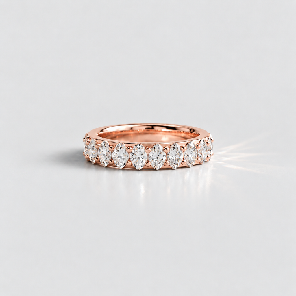A rose gold eternity ring featuring a row of marquise-cut diamonds, photographed on a clean light gray background with a soft reflection and a light flare.