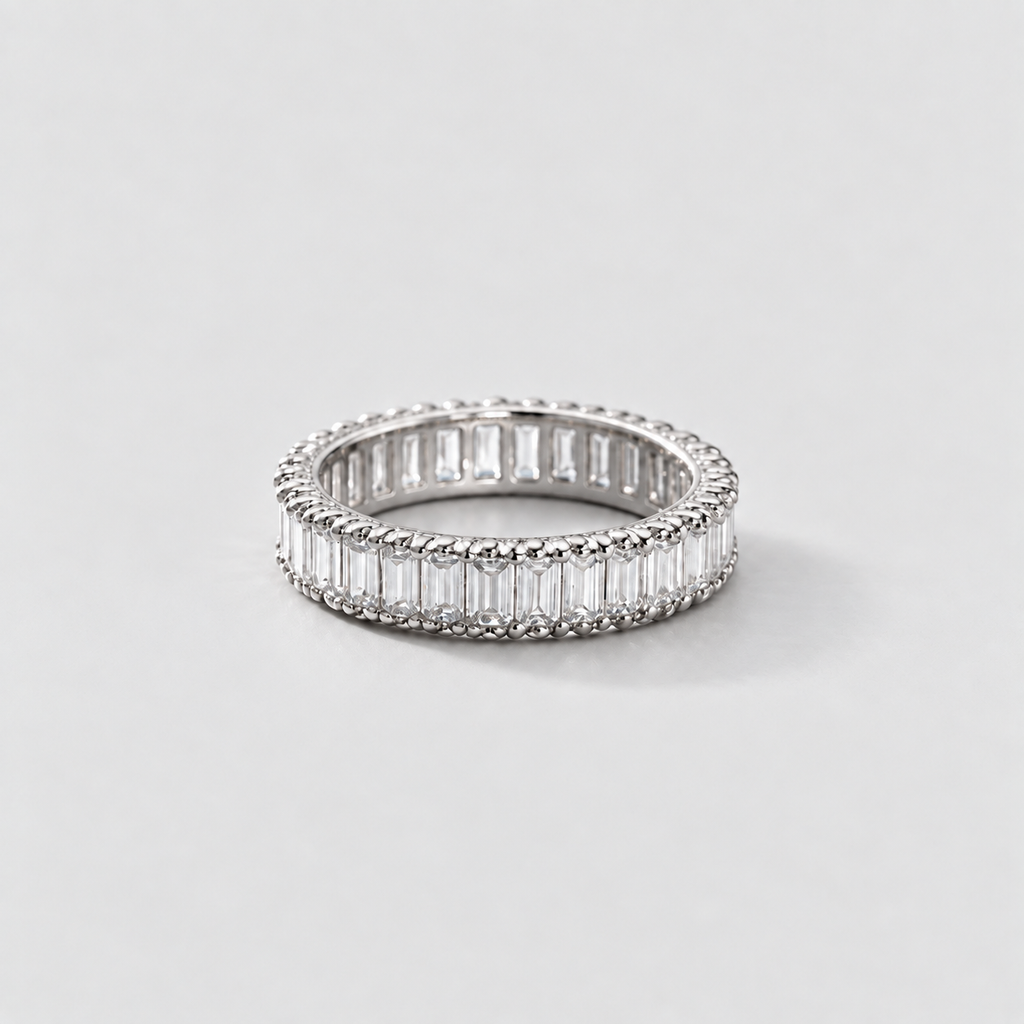 A silver eternity ring featuring baguette-cut clear stones, photographed on a clean, light gray background.