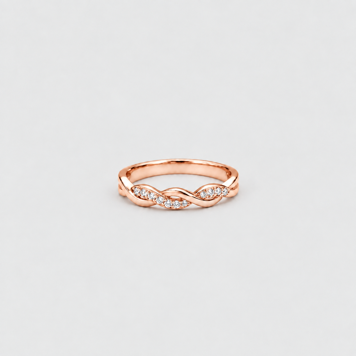 A rose gold infinity band ring with small clear pavé diamonds along the front, shown on a light gray background.