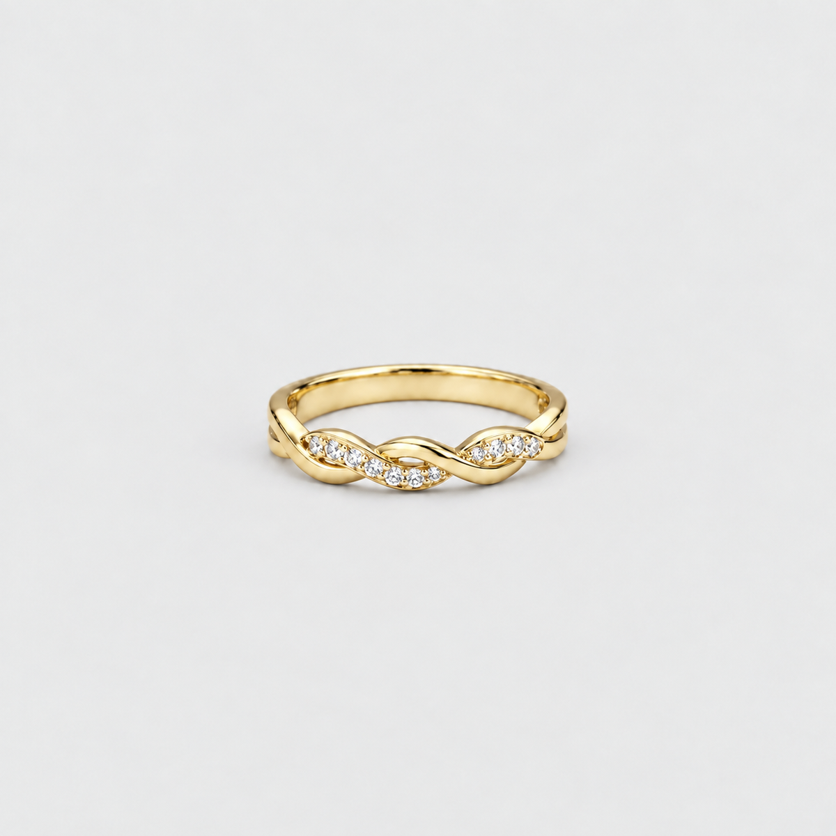 A gold band ring featuring a central twisted infinity design accented with small clear pavé diamonds, set against a clean light gray background.